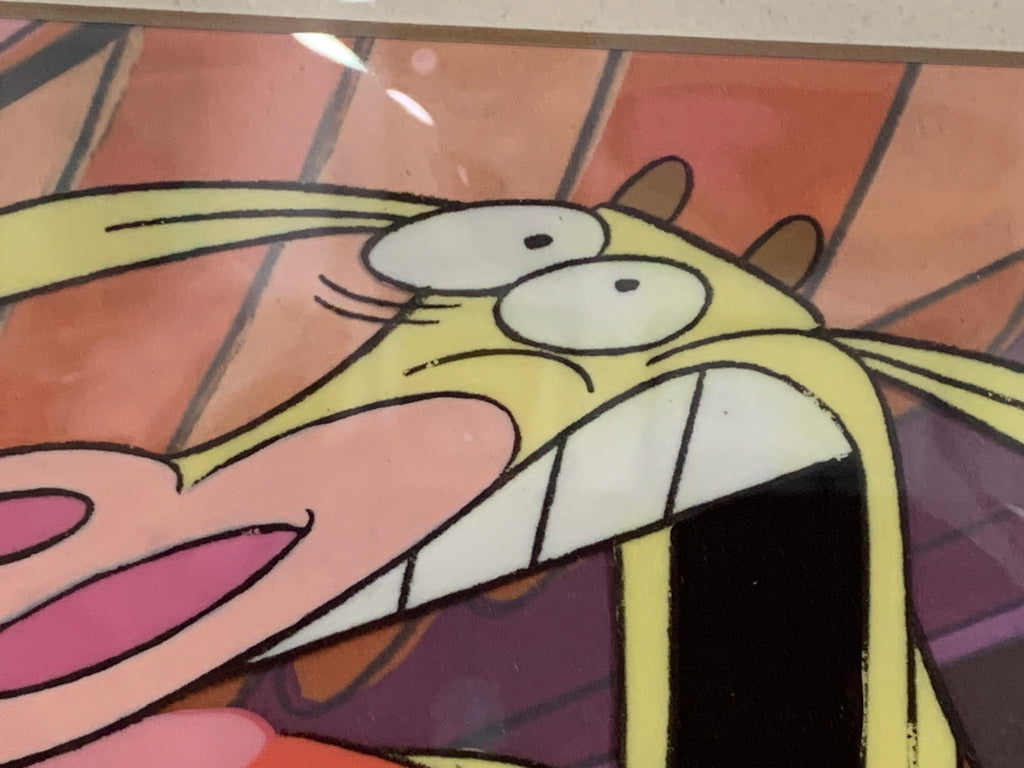 A close-up of a colourful cartoon print or artwork featuring Cow and Chicken with large white eyes, pink lips, and a black mouth area against a warm orange and pink striped background.