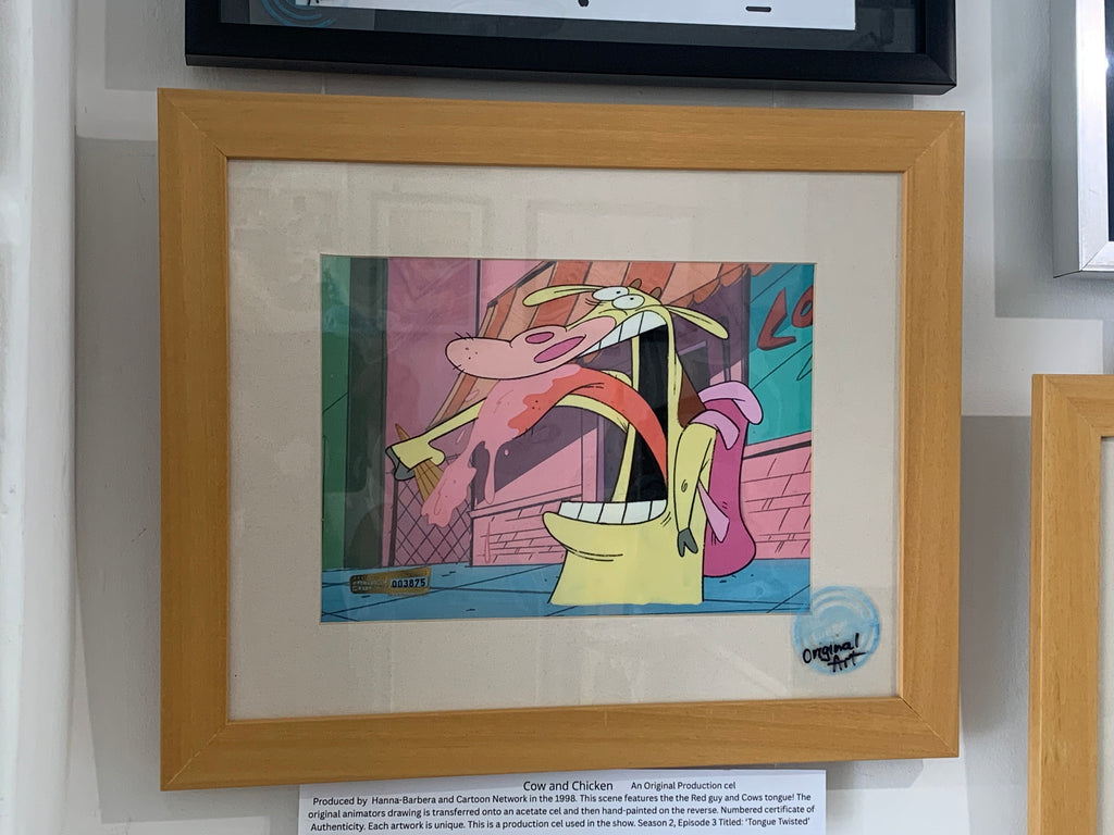 A framed vintage animation drawing from 'Cow and Chicken' displayed on a wall. The collectible colored pencil/ink drawing features the characters  in a colorful scene, mounted in a light wood frame with a white mat.