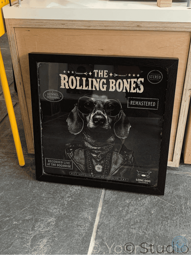 Framed album cover of 'The Rolling Bones' on a floor next to a wooden cabinet.