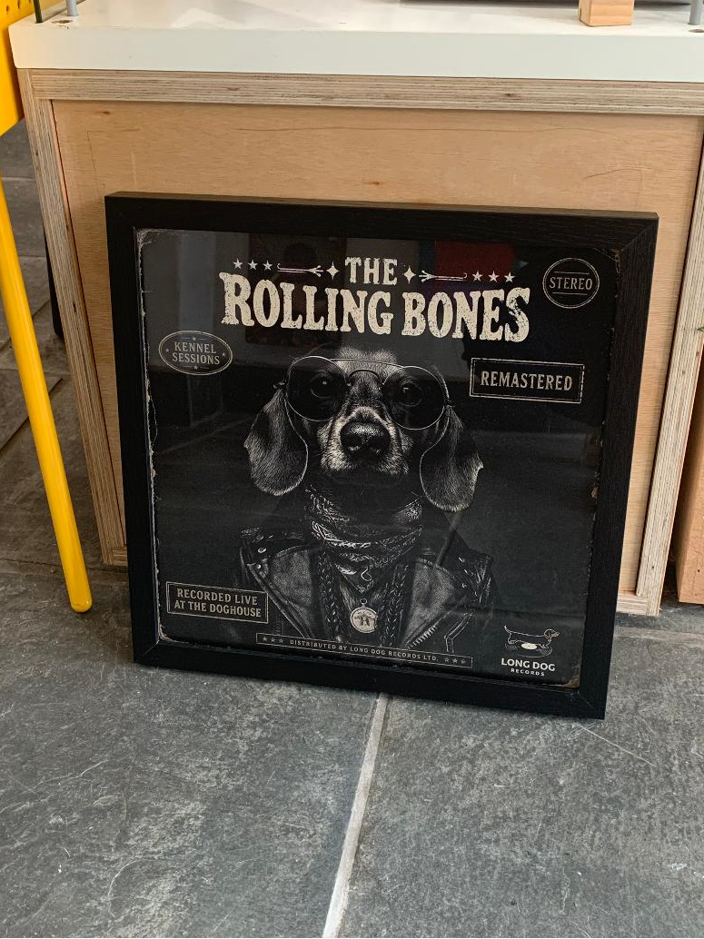 Framed album cover of 'The Rolling Bones' on a floor next to a wooden cabinet.