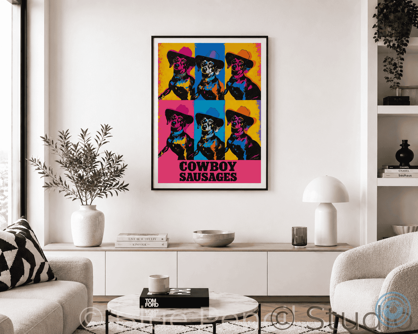A framed pop-art poster featuring six colourful cowboy sausage Dogs hangs on a white wall in a modern living room setting with a sofa, side table, lamp, and shelving.