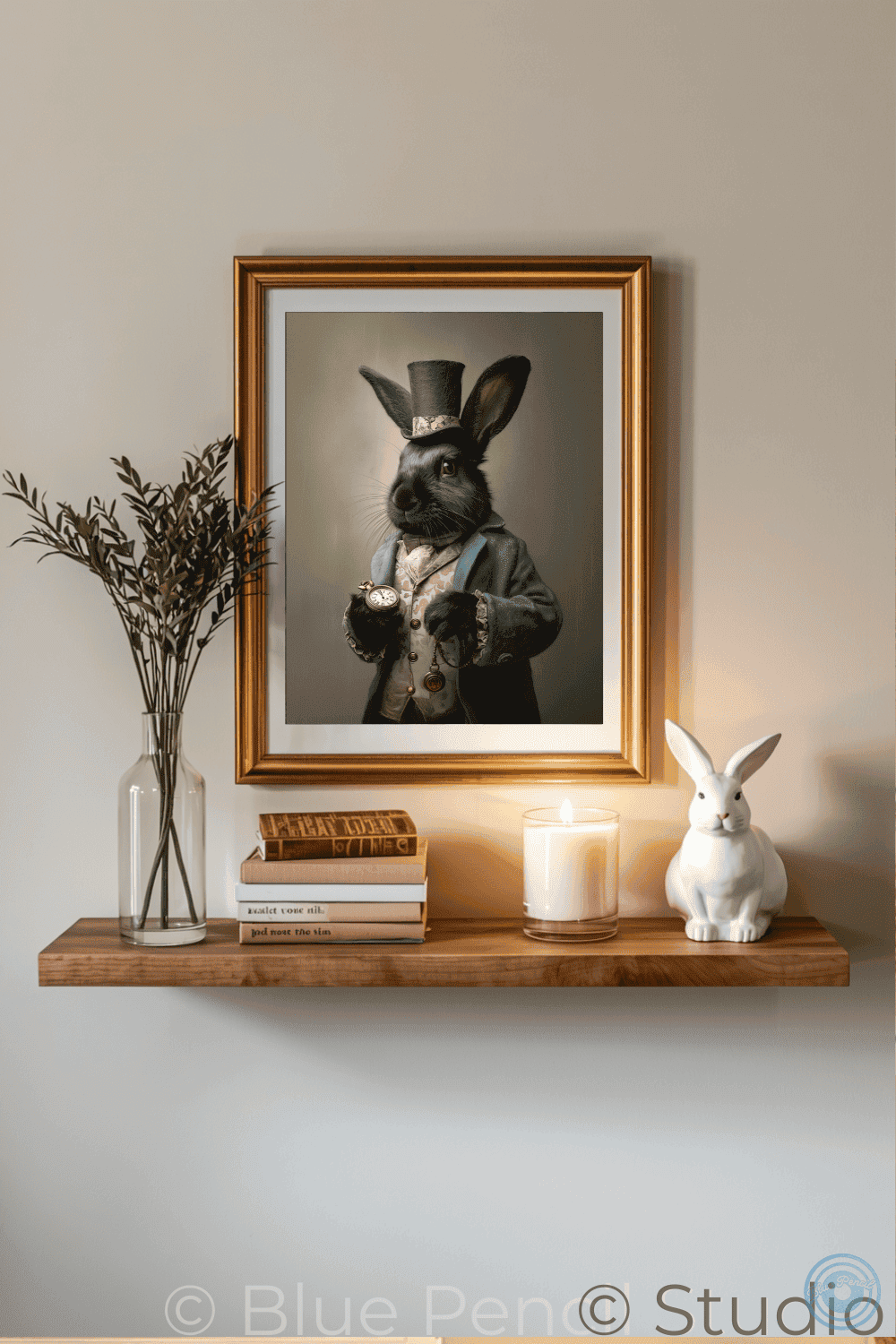 A framed art print of a rabbit dressed in vintage formalwear hangs on a wall above a wooden shelf styled with books, a candle, a white rabbit figurine, and a vase with dried stems.